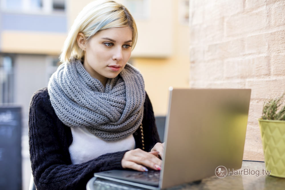 Beautiful young woman wearing tube scarf while working on laptop at outdoor cafe